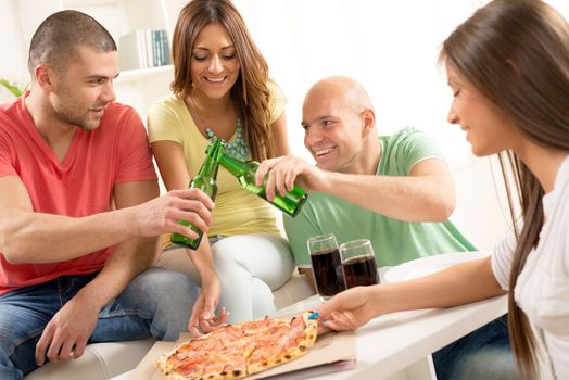 Friends enjoying eating pizza and drink a beer together at home party.