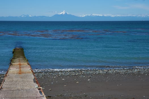 Jetty jutting out into the sea from the Island of Chiloe towards the snow capped mountains and the Corcovado Volcano on the mainland of Chile.