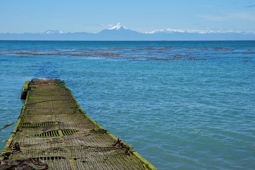 Jetty jutting out into the sea from the Island of Chiloe towards the snow capped mountains and the Corcovado Volcano on the mainland of Chile.