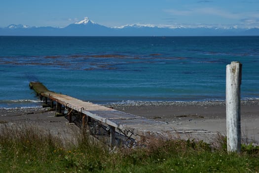 Jetty jutting out into the sea from the Island of Chiloe towards the snow capped mountains and the Corcovado Volcano on the mainland of Chile.