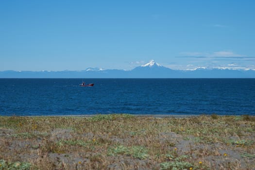 View over the sea from the Island of Chiloe towards the snow capped mountains and the Corcovado Volcano on the mainland of Chile.