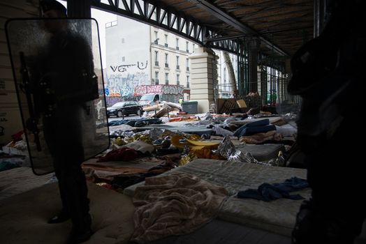 FRANCE, Paris : Police officers and gendarmes stand guard as they evacuate migrants and refugees from a makeshift camp under the Stalingrad railway station in Paris on March 30, 2016 where hundreds of migrants and refugees were established for three weeks.Launched at 6:20 (4:20 GMT) by State services, the Town of Paris and police headquarters, the operation ended peacefully two hours later. It is the 18th operation of this kind organised in the French capital since June 2015.