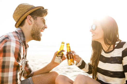 Young couple at the beach having fun, laughing and drinking beer