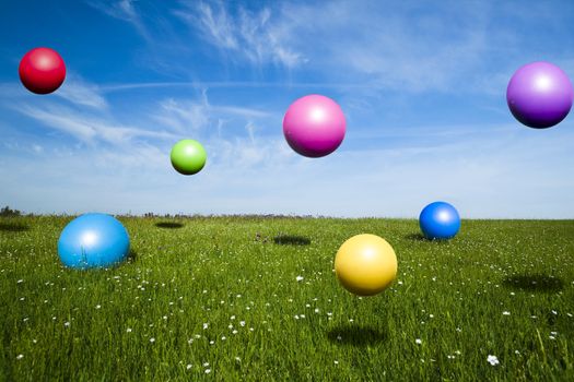 Colored balls jumping on a green meadow