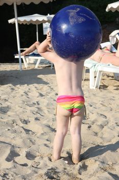 Baby girl on the beach holding big blue ball