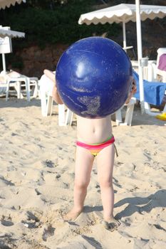 Baby girl on the beach holding big blue ball