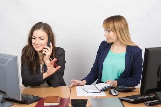 The girl in the office talking on the phone asking a colleague to wait