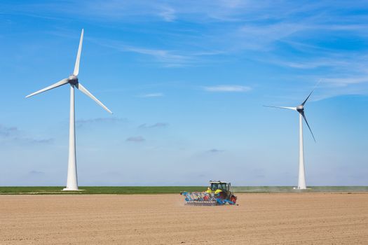 Farmer on tractor sowing in soil near dike and two windmills in the netherlands