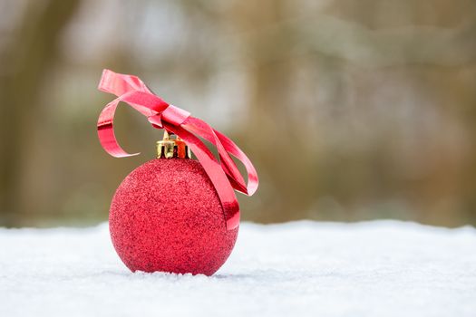 Red christmas bauble with bow outdoors on white snow