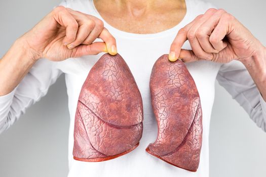 female person holding two artificial models of lungs in front of body with white shirt
