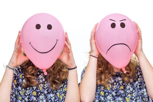 Two women holding pink balloons with happy and angry facial expressions for their heads isolated on white background
