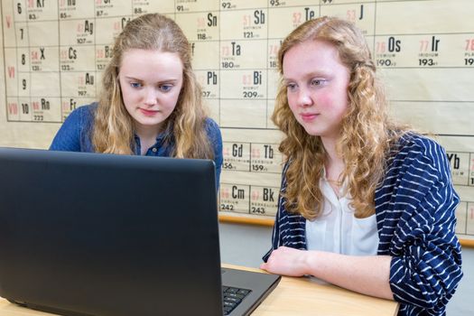 Two caucasian female students looking at computer in chemistry lesson