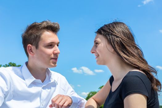 Young man and woman in love talking outdoors with blue sky