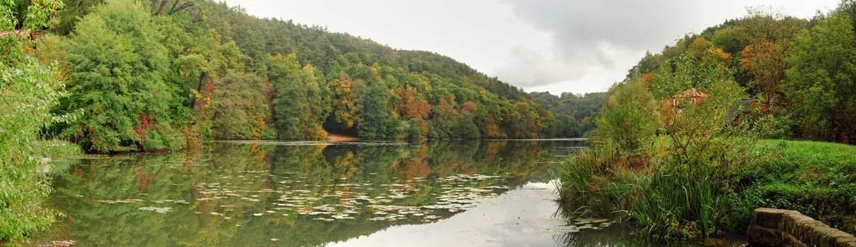 Calm surface of the lake surrounded by autumn landscape