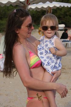 Mother and her  baby gir with glasses posing on the beachl
