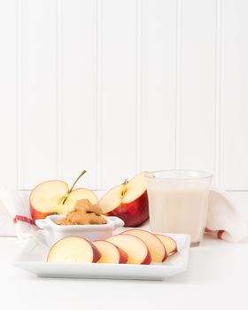 Healthy snack of fresh red apples and peanut butter with a glass of milk.