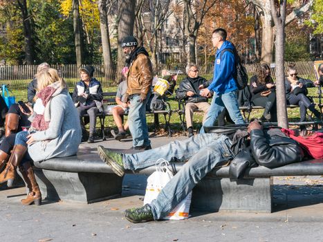 Manhattan, New York - December 06, 2015: People sitting and laying on the benches  during lazy Sunday afternoon in Washington Square Park.