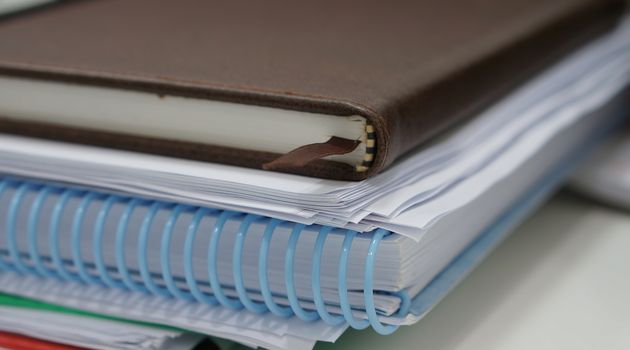 Stack of paperwork and notebook placed on white desk at office.