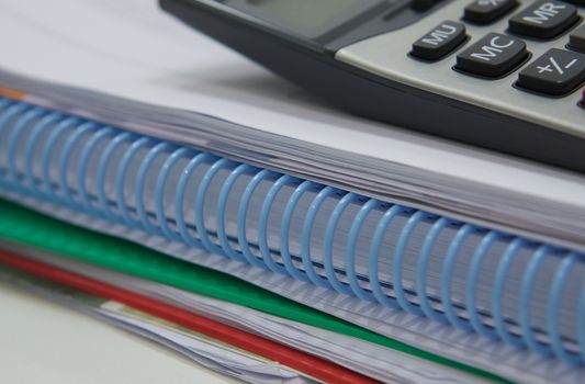 Stack of paperwork and calculator placed on desk at office.