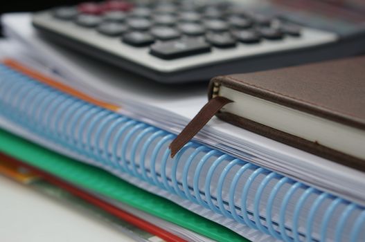 Stack of paperwork, notebook and calculator placed on desk at office room.