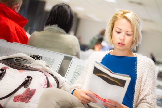 Casual blond young woman reading a magazine while waiting to board a plane at the departure gates.