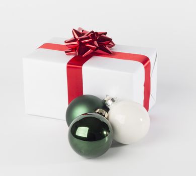 Christmas present in white paper with red ribbon and bow, green and white Christmas balls, isolated on white background