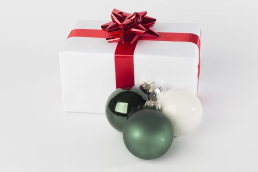 Christmas present in white paper with red ribbon and bow, green and white Christmas balls, isolated on white background