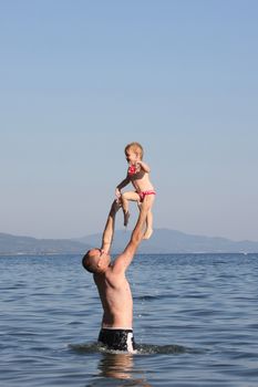 Father standing  in the water throws his baby girl 