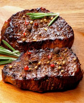 Two Gourmet Roasted Beef Steaks with Peppercorns and Coriander Seeds and Rosemary closeup on Wooden Plate