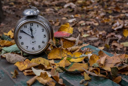 Old clock on autumn leaves on wooden table on natural background