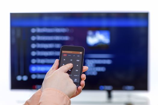 Closeup on woman hand holding smartphone and use a app with remote control  and surfing programs on television. Focus on the remote control.