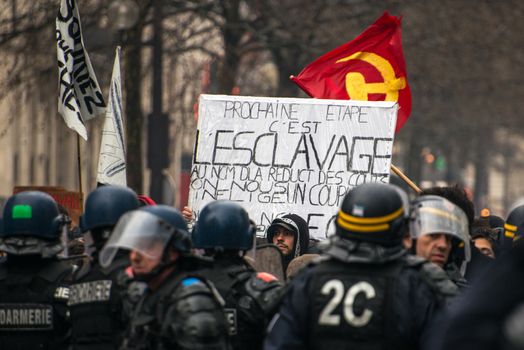 FRANCE, Paris: A protester holds a placard which reads The next step is slavery as French riot police officers stand in line as thousands demonstrate against the French government's planned labour law reforms on March 31, 2016 in Paris. France faced fresh protests over labour reforms just a day after the beleaguered government of President Francois Hollande was forced into an embarrassing U-turn over constitutional changes.