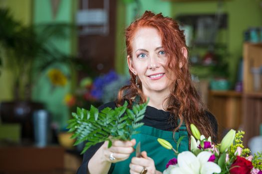 Mature adult with fern greens preparing a floral arrangement in florist shop
