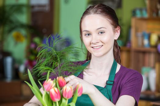 Beautiful young woman in green apron creating a tulip arrangement