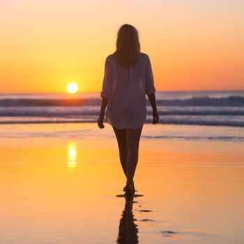 Woman walking on sandy beach in sunset leaving footprints in the sand. Beach, travel, concept. Copy space. Vertical composition.