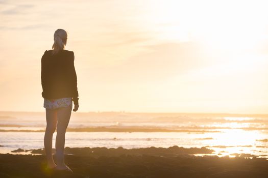 Silhouette of casualy dressed sporty woman watching sunset at the beach.