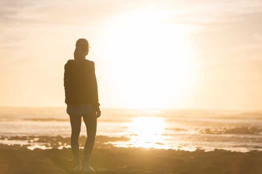 Silhouette of meditative, sensual blonde woman watching sunset at the beach.