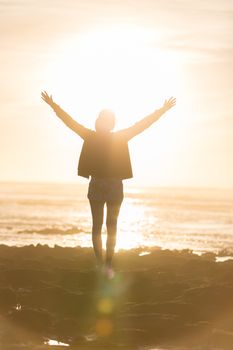 Silhouette of free woman enjoying freedom feeling happy at beach at sunset. Serene relaxing woman in pure happiness and elated enjoyment with arms raised outstretched up. 