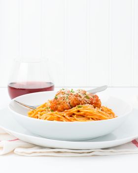 Plate of spaghetti with meatballs topped with fresh herbs and grated parmesan cheese.