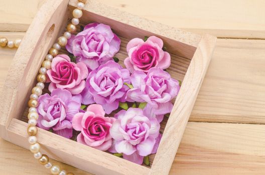Pink roses in wooden box on desk.