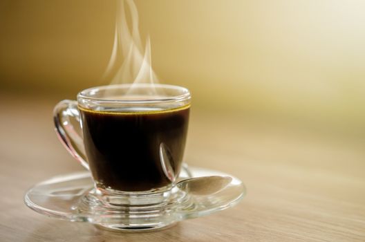 Hot black coffee in glass cup with smoke on wooden table.