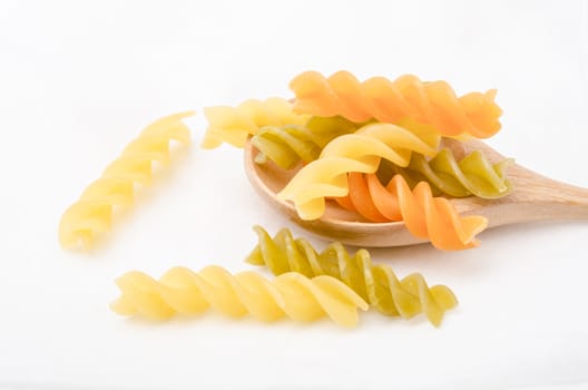 Raw colored pasta on white fabric background. Tomato, spinach and wheat