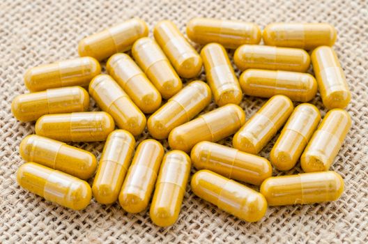 close up heap of yellow medical capsules on sack background.