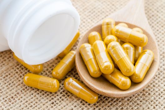 Herbal capsule spill out from bottle on sack background.