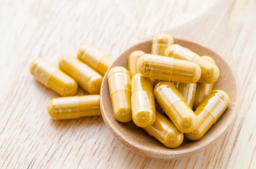 Vitamin capsules in a wooden spoon on a wooden background.