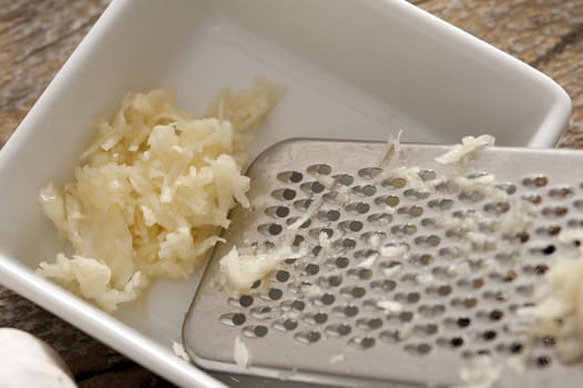 Grated fresh garlic in a small rectangular dish with a stainless steel grater at the side, high angle view