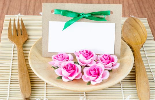 Romantic dinner table setting with blank note card and pink rose.