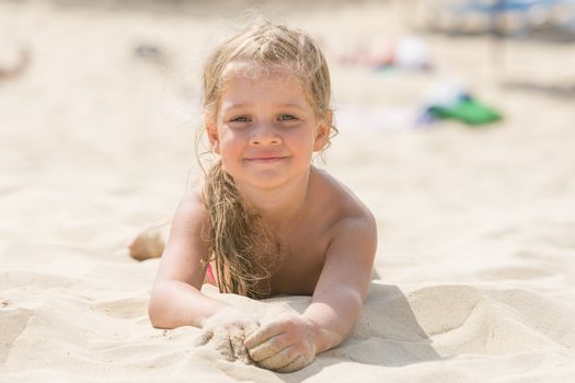 Pretty girls four years lying in the sand on his stomach on the beach on a sunny day
