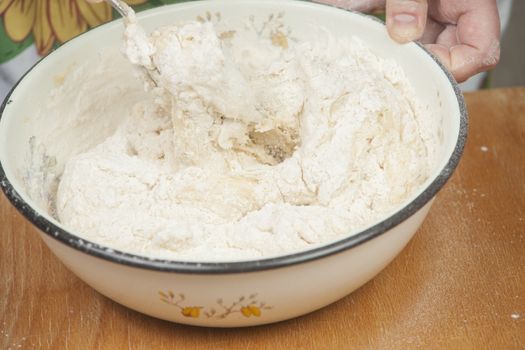 Women's hands preparing fresh yeast dough in the bowl.