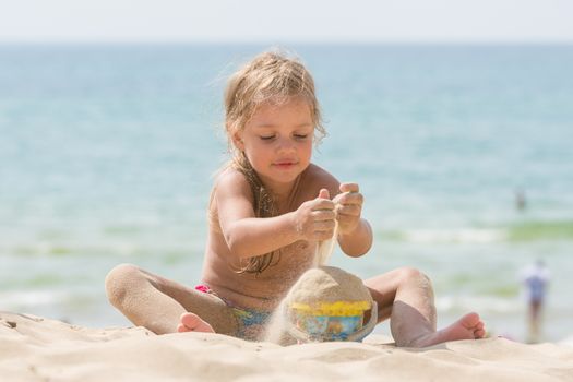 Little five-year girl pours sand into bucket baby on the sea beach